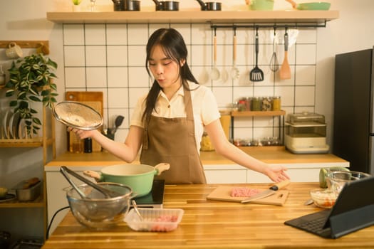 Asian woman checking a pot of boiling water while cooking spaghetti in a stylish kitchen.