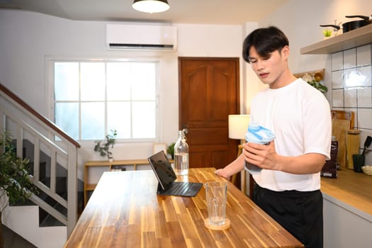 Young man standing in a kitchen preparing protein shake after a workout.