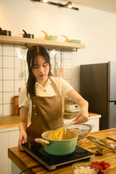Smiling woman lifting boiled spaghetti from steaming pot while preparing a delicious homemade dish.