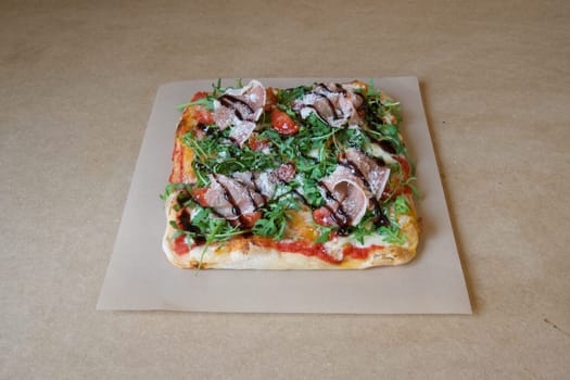 A pizza with basil and tomatoes on it. The pizza is on a brown paper