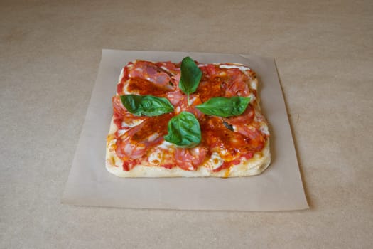A pizza with basil and tomato sauce on top. The pizza is on a brown table. The pizza is cut into four pieces
