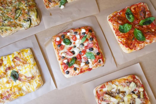A variety of small pizzas are displayed on a table, each with different toppings. The pizzas are arranged in a grid, with some placed closer to the front and others towards the back