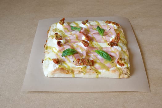 A pizza with ham, cheese, and basil on top. The pizza is sitting on a brown table