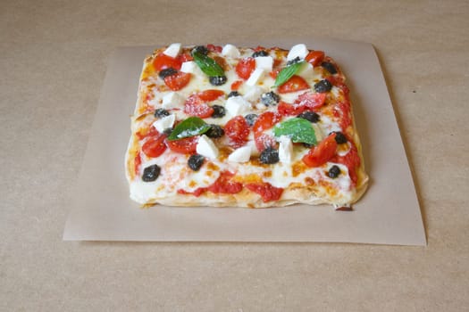A pizza with cheese, tomatoes, and basil on top. The pizza is sitting on a brown paper