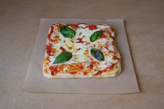 A pizza with basil leaves on top of it. The pizza is sitting on a brown paper. The pizza is cut into squares