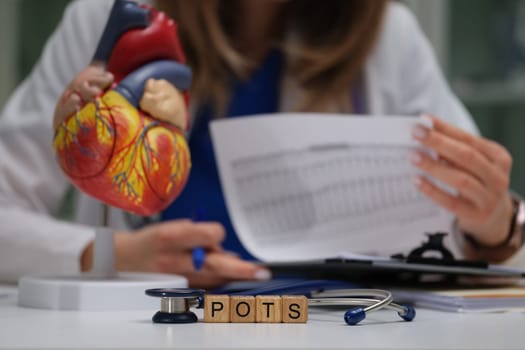 A medical professional meticulously reviews extensive data regarding POTS while a heart model is present nearby