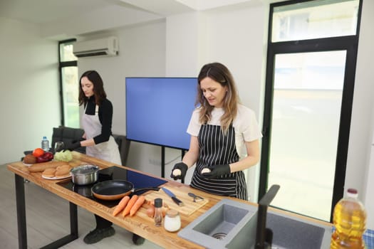 In a stylish, modern kitchen, two women are busily preparing food with a variety of vibrant, fresh ingredients