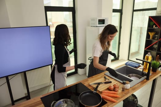 Two women are joyfully cooking together in a modern kitchen, showcasing their teamwork and culinary skills