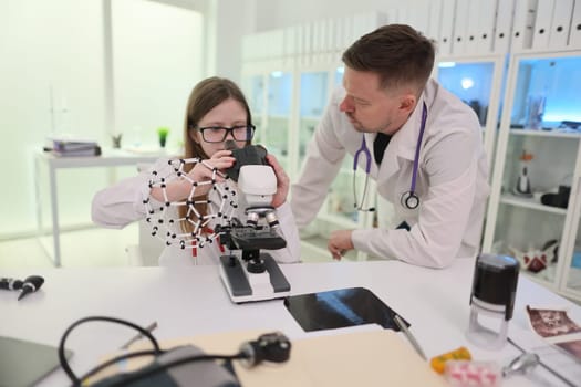 A young girl is using a microscope while a professional adult effectively guides her in a lab setting