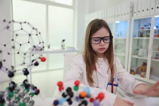 A young girl scientist, dressed in a lab coat, diligently works with intricate molecular models in her lab