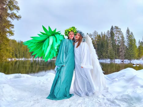 Two girls in white and green attire pose at a lake, symbolizing the shift from winter to spring in nature.
