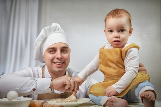 A family enjoys a fun cooking session, playfully covered in flour while engaging with their little ones in a warm kitchen. Father and son having fun