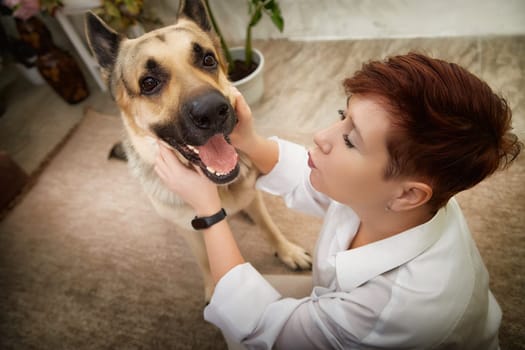 Blonde woman interacts lovingly with her German Shepherd dog in a comfortable home environment, capturing a warm moment.