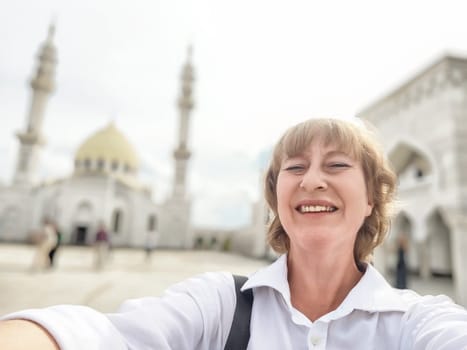 Smiling traveler captures a joyful selfie in front of a beautiful mosque while exploring the area on a sunny day.