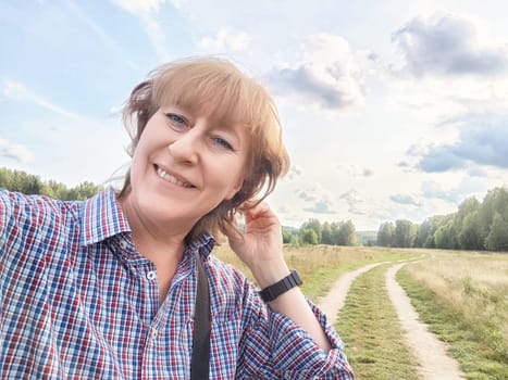 A female traveler captures a joyful selfie while exploring a scenic path surrounded by greenery on a sunny day.