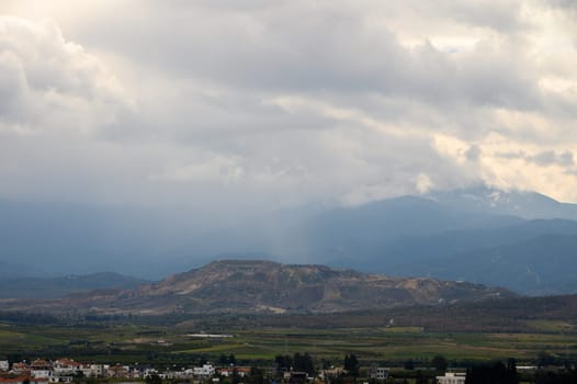 Dark clouds roll over rolling hills and valleys, creating a moody atmosphere in a peaceful rural setting.