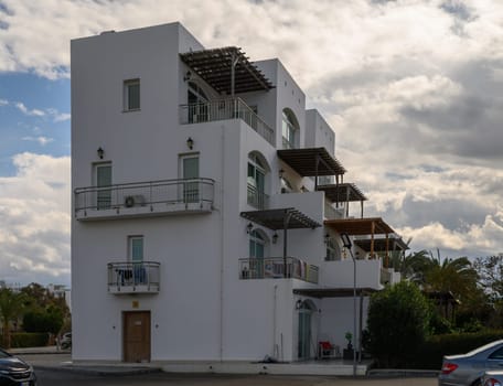 A contemporary white building showcases balconies and greenery, creating a tranquil atmosphere by the sea.