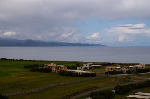 Gentle waves lap against the shore as quaint houses overlook the beautiful expanse of the ocean and distant mountains.