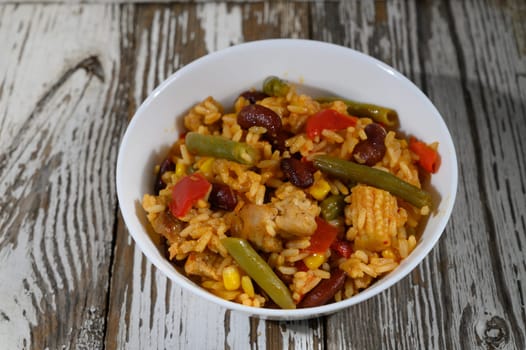 A colorful combination of rice, beans, and fresh vegetables presented in a charming bowl on a weathered wooden table.
