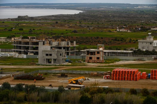 Workers engage in building activities amid scenic views of the coast and lush fields, highlighting local development.