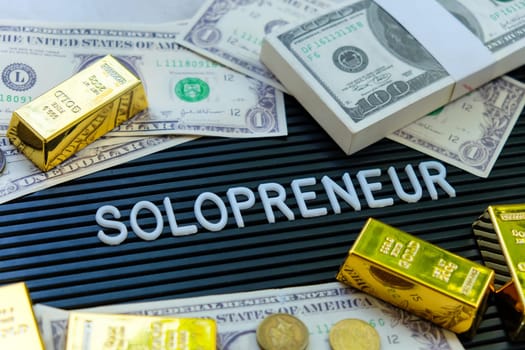 Business concept. Gold bars and dollars on a black background with the word solopreneur.