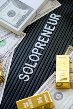 Business concept. Gold bars and dollars on a black background with the word solopreneur.
