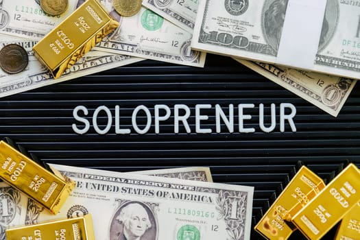 Business concept. Gold bars and dollars on a black background with the word solopreneur.