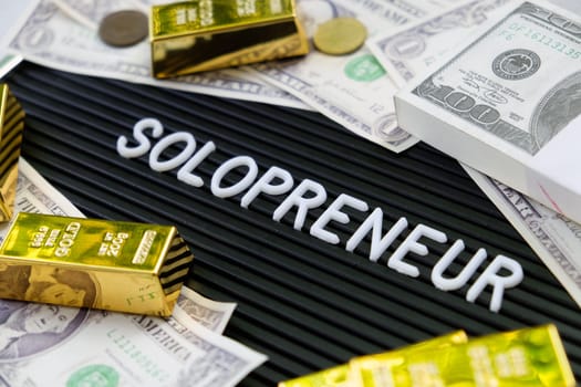 Business concept. Gold bars and dollars on a black background with the word solopreneur.
