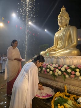 A devotee offers flowers at the Buddha statue during a peaceful evening ceremony. Isolated on white background.