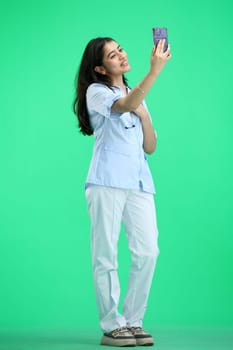A woman doctor, full-length, on a green background, talking on the phone.