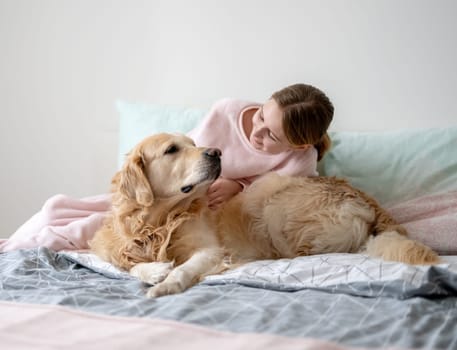 Cute Little Girl Petting And Playing With Lovely Golden Retriever Dog In Bed