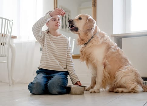 Happy Smiling Girl Sitting On A Floor Feeding And Playing With An Adorable Golden Retriever Dog At Home