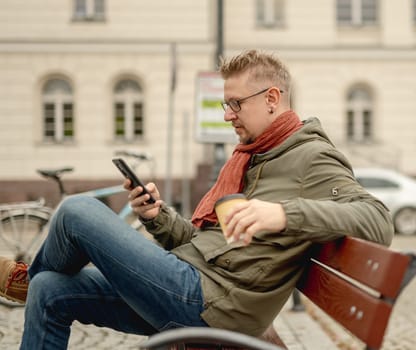 Stylish Man On City Bench Drinking Coffee Browsing Internet