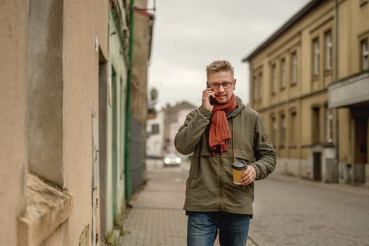 Attractive Stylish Man Walks On The City Street, Talking On The Phone And Drinking Coffee