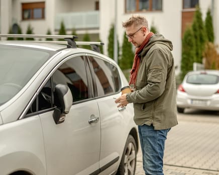Young Attractive Man Parks A Car On A Street And Opens The Car With A Key In An Autumn City