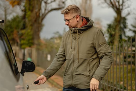 Young Attractive Man Stands On The Street With A Car, Opening The Car Door With A Key