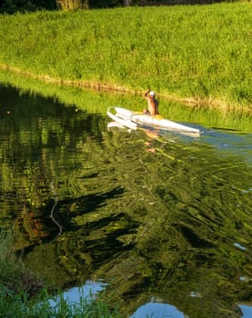 A man paddles a traditional Hawaiian outrigger canoe through the tranquil waters of Hanalei River on a sunny day, creating mirrored reflections.