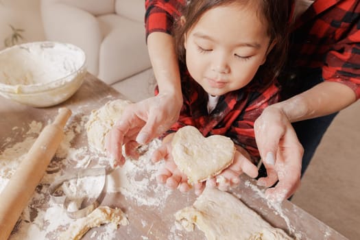 Mother and child baking together, hands holding heart-shaped dough, family bonding, homemade pastry, cozy kitchen scene, flour-covered hands.
