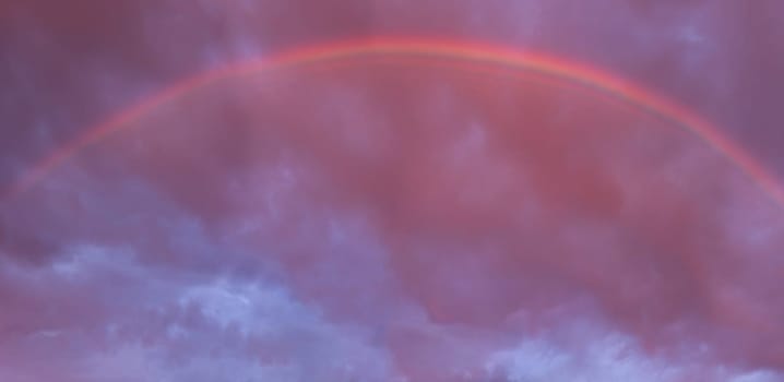 Beautiful rainbow appearing on cloudy sky during a breathtaking sunset, creating a magical atmosphere