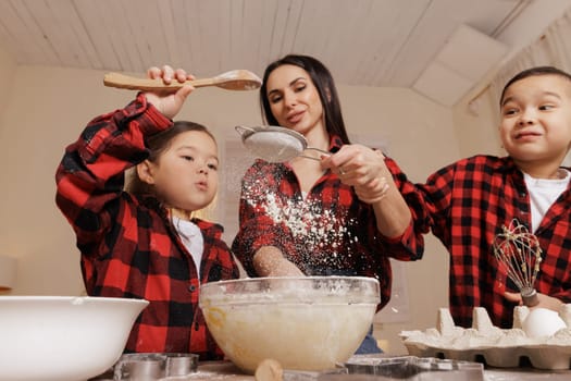 Mother and kids baking together, sifting flour, playful cooking moment, family bonding, homemade treats, kitchen fun, childhood joy, festive atmosphere.