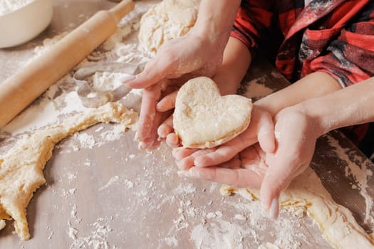 Mother and child baking together, hands holding heart-shaped dough, family bonding, homemade pastry, cozy kitchen scene, flour-covered hands.