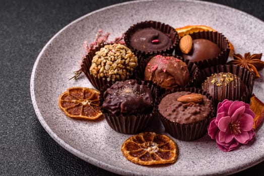 Homemade chocolate candies with different fillings and sprinkles on a dark concrete background