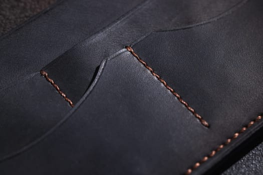 Close up of a black leather wallet highlighting the copper stitching and multiple pocket compartments, suggesting high quality craftsmanship