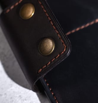 Brown thread stitching detail on dark leather with brass rivets, showcasing craftsmanship
