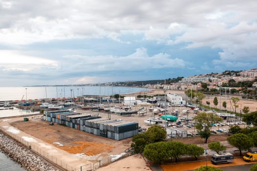 Drone view captures cargo containers arranged at commercial dock in Alges District, Lisbon. The scene highlights bustling activity and efficiency of port by Tagus River against cloudy sky