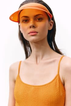 Confident young woman wearing a colorful orange top and sporty visor, set against a simple white background, ideal for summer fashion and lifestyle themes.