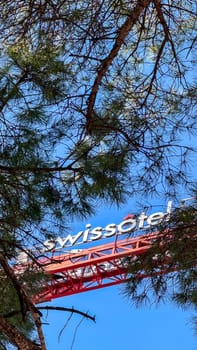 22.02.2025.Budva,Montenegro.Swissotel sign on crane boom partially visible behind tree branches, with red structure against clear blue sky.