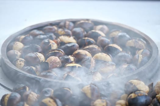 Chestnuts are being roasted, emitting steam and smoke in a market.