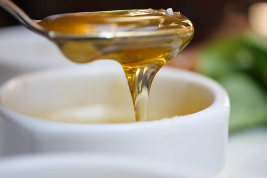 Honey flows from a spoon into a white bowl, creating a delicious look.