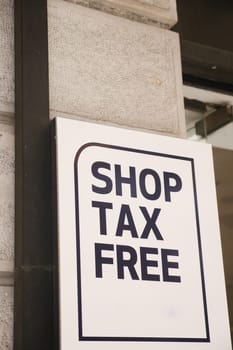 Sign promoting tax-free shopping hangs on a building in a bustling area.